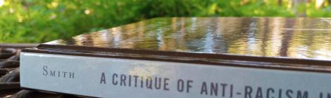 A photo of Erec Smith's book A Critique of Anti-Racism in Rhetoric and Composition, sitting on a picnic table, with green leaves in the background
